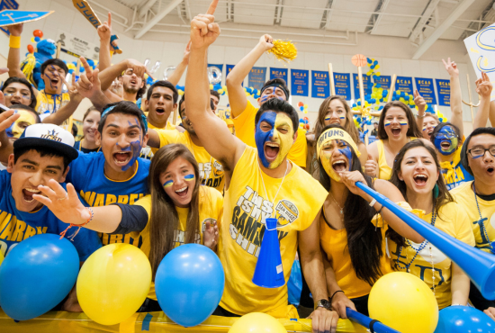 Students in UC San Diego shirts and blue and gold face paint cheering at an athletics game.