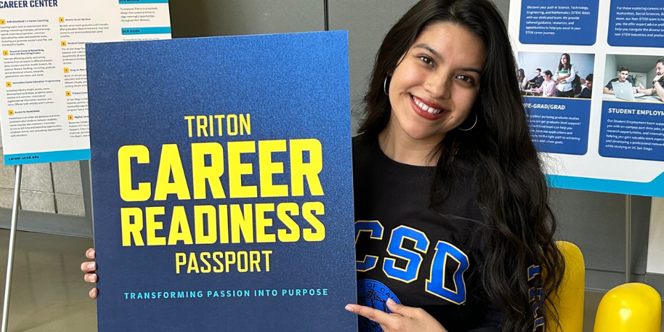 Student in UCSD sweatshirt smiling and holding Career Readiness Passport poster.