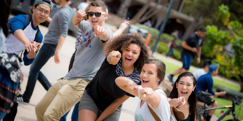 Group of students smiling and pointing at the camera excitedly.